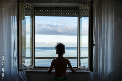 Italy. Minturno. A child in front of a window overlooking the sea.