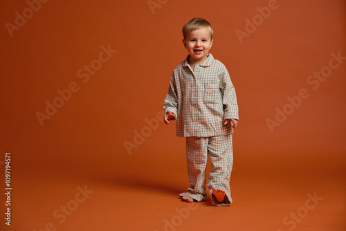 Canvas Print A young child smiles brightly while standing on an orange backdrop, dressed in cozy pajamas