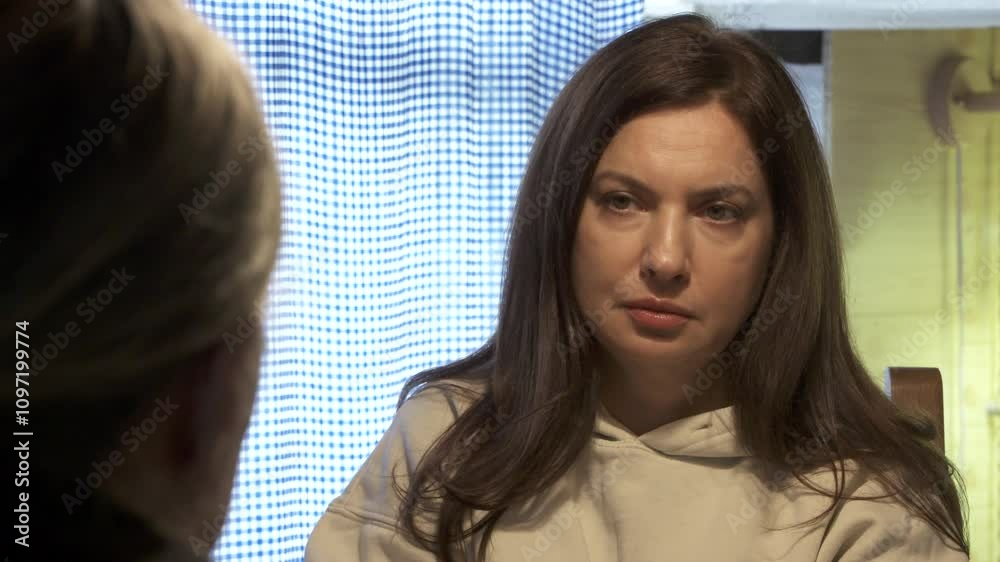 Adult 44 year old woman having lively conversation with elderly woman sitting at table in living room. Woman with tense face listens and talks with her interlocutor.