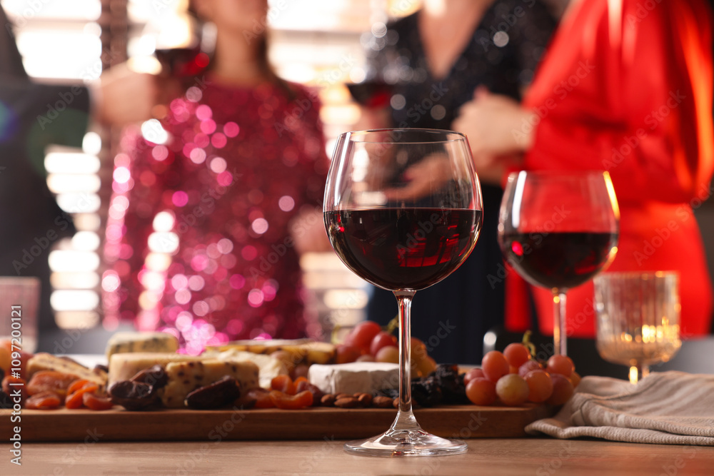 People holding glasses of wine at party, focus on wooden table with snacks and alcohol People holding glasses of wine at party, focus on wooden table with snacks and alcohol