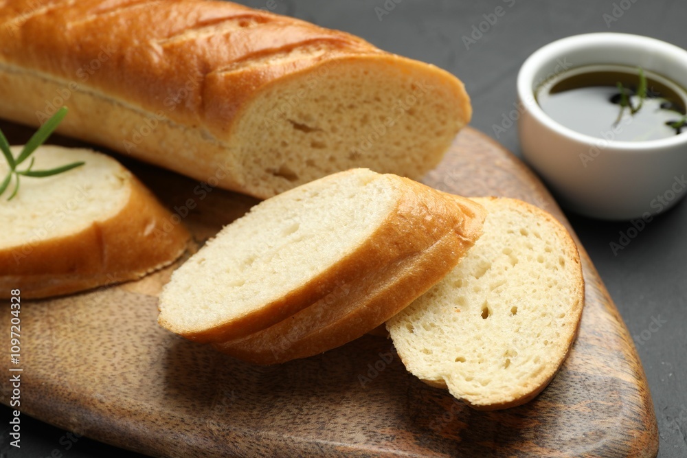 Cut fresh baguette with balsamic and rosemary on black table, closeup Cut fresh baguette with balsamic and rosemary on black table, closeup
