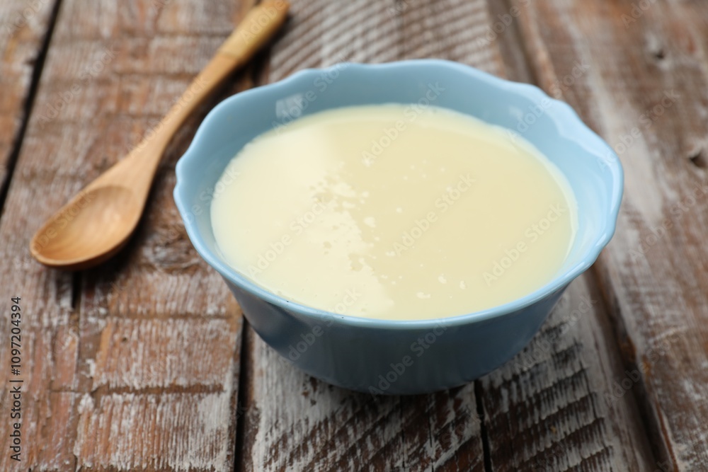 Condensed milk in bowl and spoon on wooden table, closeup Condensed milk in bowl and spoon on wooden table, closeup