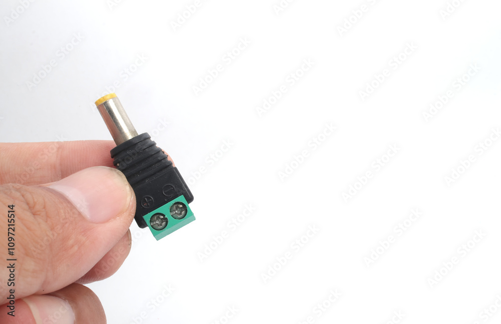 A male DC jack with green screw connection held in hand on white background. A male DC jack with green screw connection held in hand on white background.