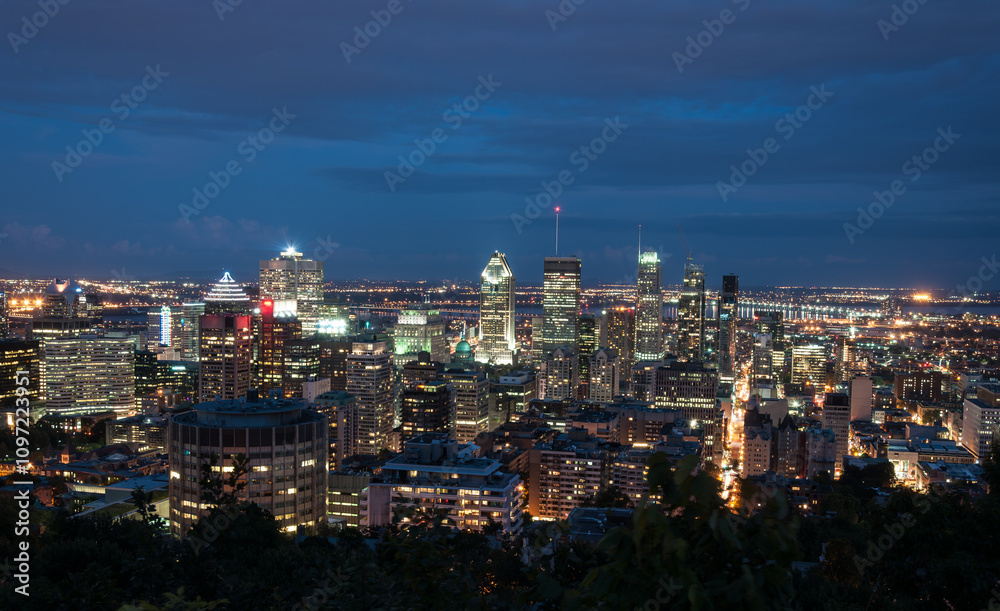 Obraz premium Stunning nighttime view of downtown Montreal, Canada, with illuminated skyscrapers and vibrant city lights under a deep blue sky. Perfect for urban and travel themes.