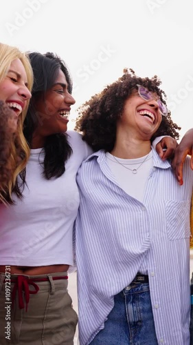 Vertical. Large group of multiracial young only women standing embracing in circle laughing outdoor. Gen z cheerful female community friends people hugging together having fun enjoying leisure time