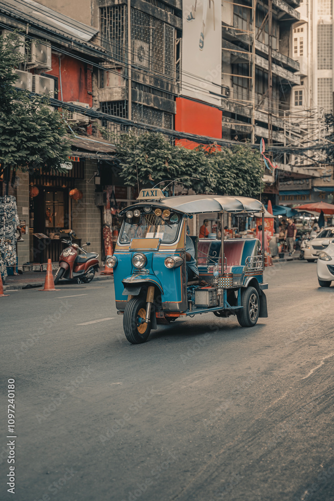 Obraz premium Busy urban street in Southeast Asia featuring traditional tuk-tuks lined up in traffic. The scene captures the vibrant local culture, with bustling markets, pedestrians, and vintage architecture.