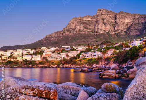 Evening view of Bakoven and Camps Bay with lights reflecting in the Atlantic Ocean, from Beta Beach, Cape Town, South Africa
