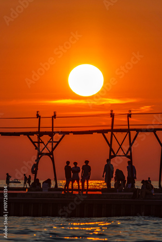 People silhouetted against a dark orange sky as the sun sets behind the Grand Haven pier in Michigan