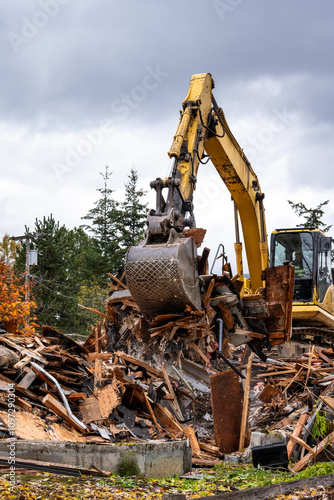 Large yellow excavator working piling up the remains of house demolition, rainy day residential construction project job site 