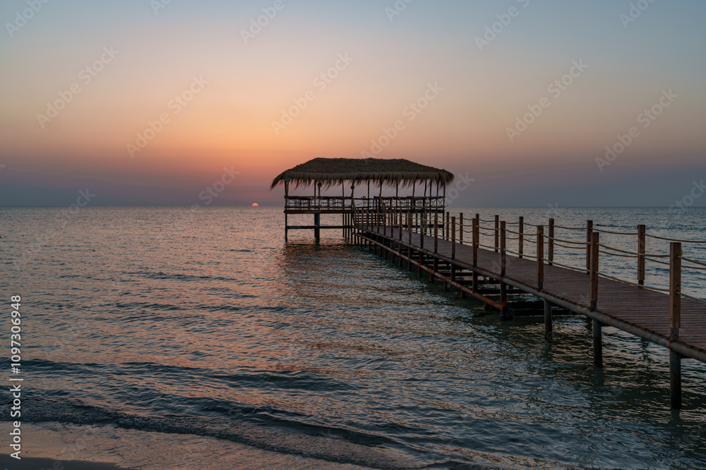 Fototapeta premium A beautiful view of the sunrise, sunset over the sea horizon with a pier in the foreground