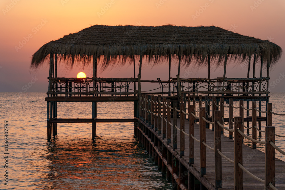 Obraz premium A beautiful view of the sunrise, sunset over the sea horizon with a pier in the foreground