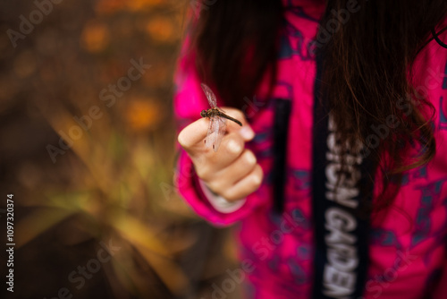 A girl holds a dragonfly in her hand in a pink coat