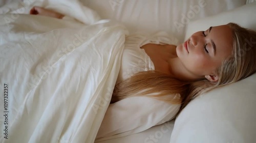 Peaceful blonde girl with fair skin sleeping in white nightdress on her bed at night.