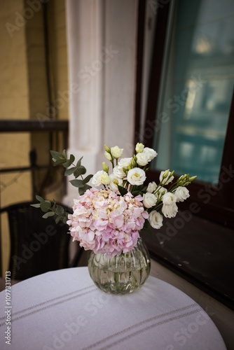 Bouquet of ranunculus blooms in a glass vase standing on a white table on a french balcony in the evening with street lights on its background in spring in Kyiv photo