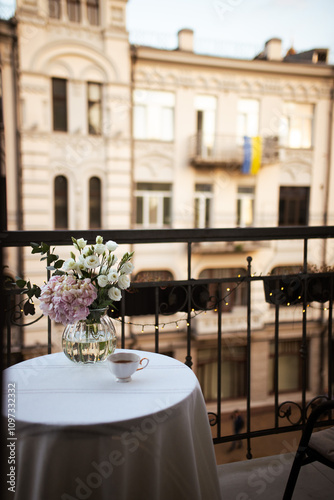 Bouquet of ranunculus blooms in a glass vase standing on a white table on a french balcony in the evening with street lights on its background in spring in Kyiv photo