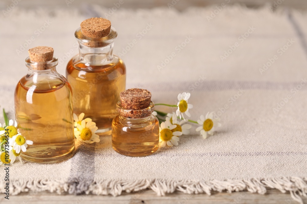 Bottles of essential oil and chamomile flowers on table, closeup. Space for text Bottles of essential oil and chamomile flowers on table, closeup. Space for text