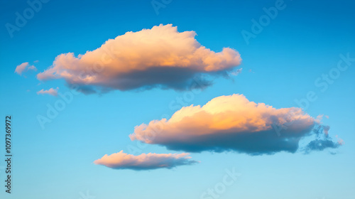 Subtle pink clouds tinged with yellow hues floating across a cool blue sky just after sunrise photo