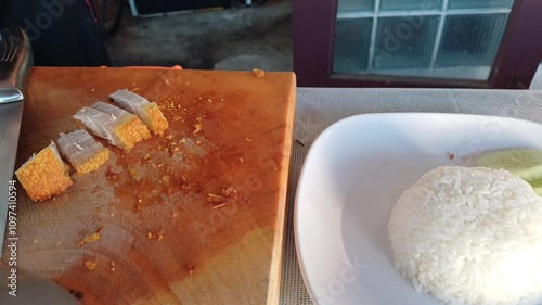 A cook is preparing crispy pork with rice, a popular Thai street food. 