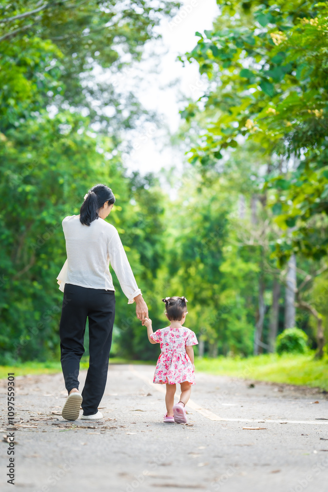 A mother carries her little daughter through a green space surrounded by trees. They enjoy fresh air, outdoor fun, and quality time together, embracing nature on a beautiful sunny day A mother carries her little daughter through a green space surrounded by trees. They enjoy fresh air, outdoor fun, and quality time together, embracing nature on a beautiful sunny day