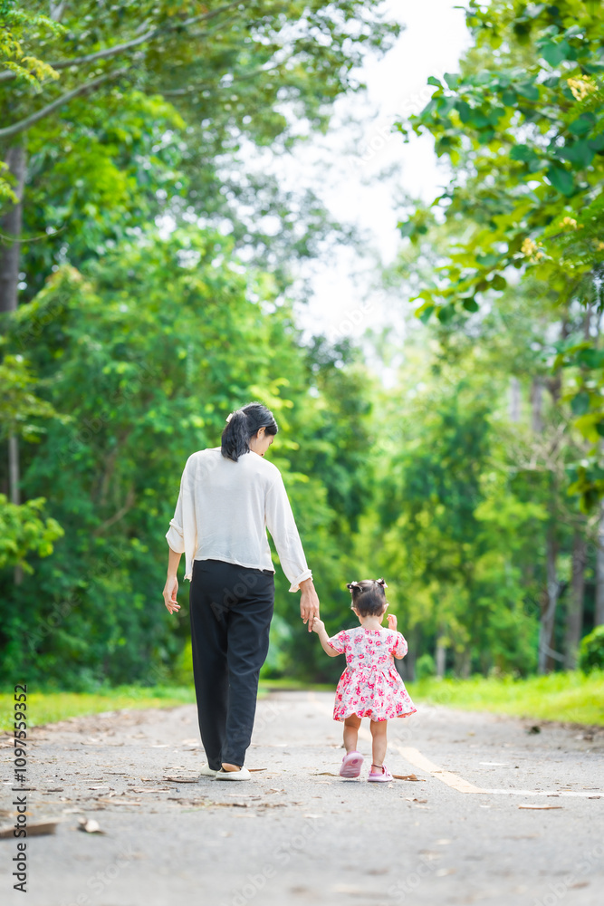A mother carries her little daughter through a green space surrounded by trees. They enjoy fresh air, outdoor fun, and quality time together, embracing nature on a beautiful sunny day A mother carries her little daughter through a green space surrounded by trees. They enjoy fresh air, outdoor fun, and quality time together, embracing nature on a beautiful sunny day