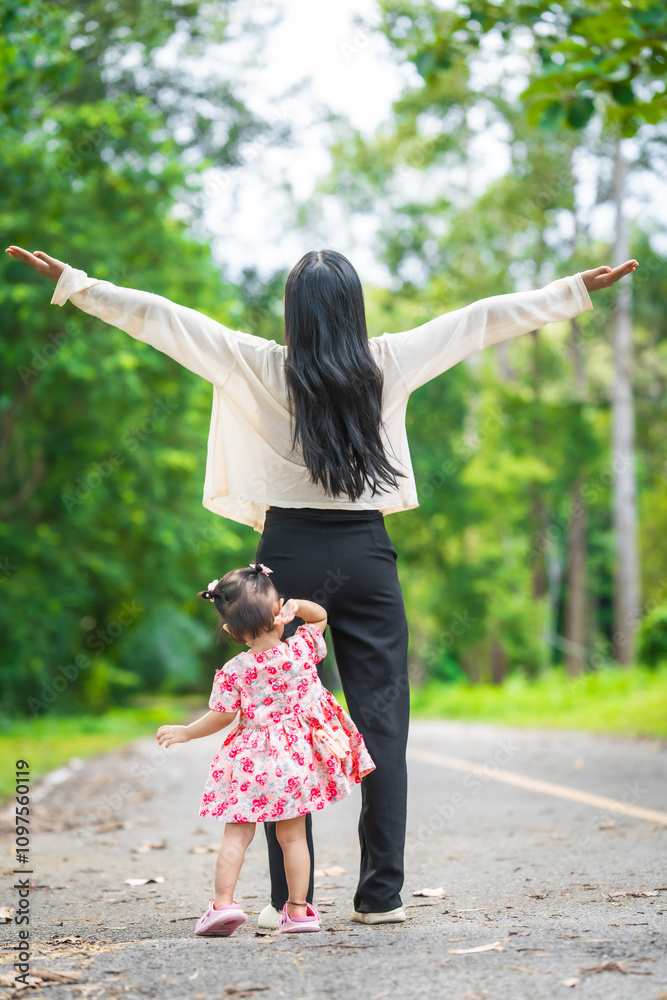Obraz premium A mother carries her little daughter through a green space surrounded by trees. They enjoy fresh air, outdoor fun, and quality time together, embracing nature on a beautiful sunny day