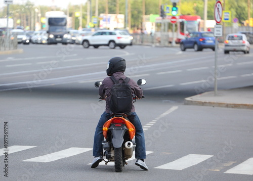 A motorcyclist stands at a pedestrian crossing at an intersection, Novocherkassky Prospekt, Saint Petersburg, Russia, July 26, 2024 photo