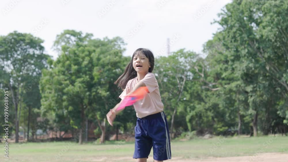 A cute Asian elementary school girl is playing with colourful windmills in a green park. With different poses and perspectives, when the wind hits the windmill, it spins beautifully. Children love it. A cute Asian elementary school girl is playing with colourful windmills in a green park. With different poses and perspectives, when the wind hits the windmill, it spins beautifully. Children love it.