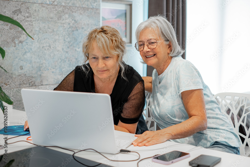 Mature confident women sitting together at home browsing on laptop while spending time looking social media, shopping online Mature confident women sitting together at home browsing on laptop while spending time looking social media, shopping online