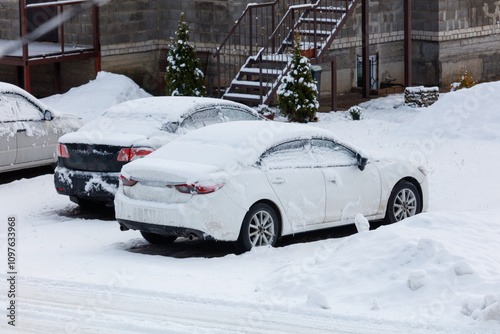 A white car is covered in snow and parked in a driveway photo