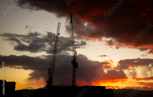 Eye level view of two luffing  jib cranes  silhouetted against a dramatic desert sunset