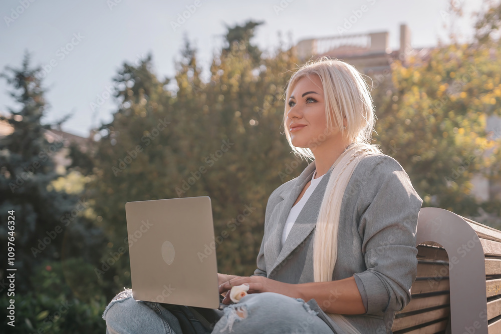 A woman is sitting on a bench with a laptop in front of her. She is smiling and she is enjoying her time. A woman is sitting on a bench with a laptop in front of her. She is smiling and she is enjoying her time.