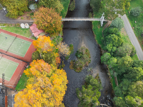 Aerial view of footbridge over a river with tennis courts and colourful Autumn trees alongside photo