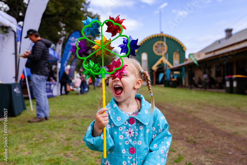 Happy little kid in blue rain jacket playing with pinwheel at local agricultural show