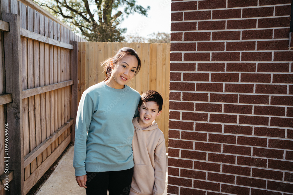 Mum and son standing outside in front of the brick wall of their house. Mum and son standing outside in front of the brick wall of their house.