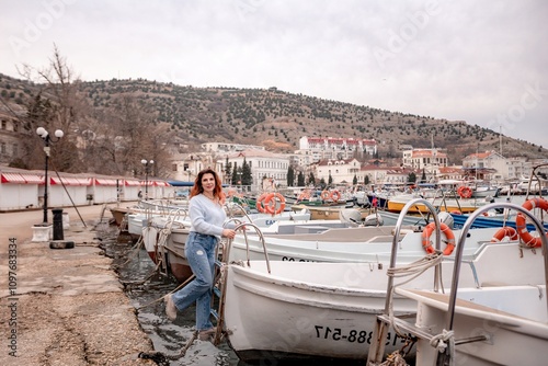 A woman stands in front of a row of boats, some of which have orange life preservers on them. The scene is peaceful and serene, with the boats and the woman creating a sense of calmness and relaxation photo