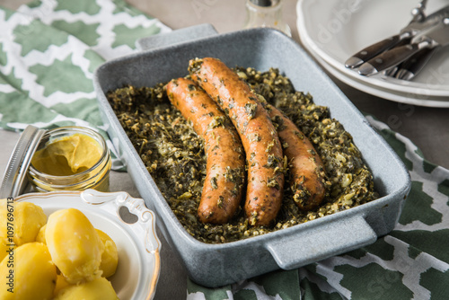 Oldenburger Grünkohl mit Pinkel Kohlwurst in Schale, Salzkartoffeln und Senf auf gedeckten grau Tisch mit grün Tuch, Teller, Besteck rustikal  photo