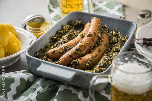 Oldenburger Grünkohl mit Pinkel Kohlwurst in Schale, Salzkartoffeln, Senf und Bier auf gedeckten grau Tisch mit grün Tuch, Teller, Besteck rustikal  photo