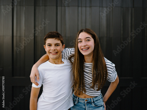 happy teen siblings standing with arms on each others shoulders against black garage door photo