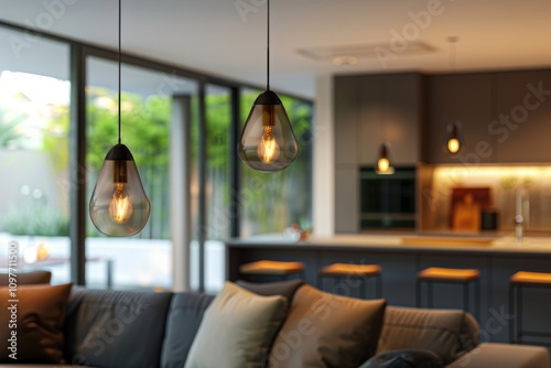 Two teardropshaped pendant lights illuminate a modern living room with a blurred kitchen background. photo