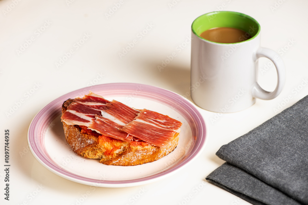 Serrano ham toast, olive oil and tomato with a cup of coffee with milk, a typical breakfast in Andalusia. White background. Serrano ham toast, olive oil and tomato with a cup of coffee with milk, a typical breakfast in Andalusia. White background.