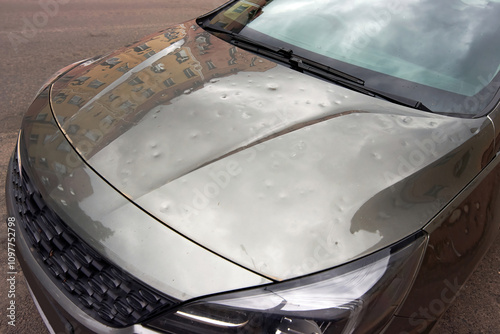 Parked car damaged by hail with visible dents on hood and cracks, need for auto repair and maintenance. Car body exterior with cosmetic damage, dents and severe impact from hailstorm