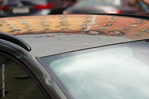 Car roof damaged by hail with visible dents and scratches on roof, aftermath of a severe weather event. Small dents in vehicle`s exterior, severe impact from hailstorm. Selective focus