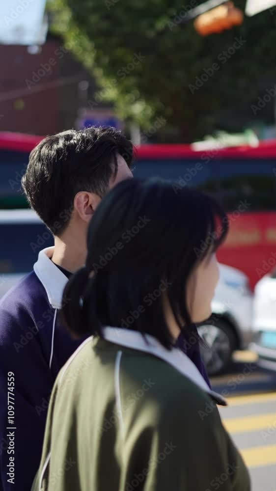 A Korean couple, a man in his 30s and a woman in her 20s, wearing tracksuits, are walking together on a public road in Seoul, South Korea. Vertical video. A Korean couple, a man in his 30s and a woman in her 20s, wearing tracksuits, are walking together on a public road in Seoul, South Korea. Vertical video.