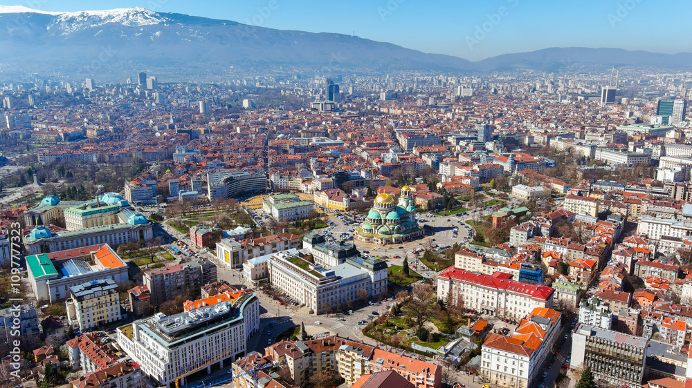 Obraz premium Aerial view of Sofia’s iconic Alexander Nevsky Cathedral amidst a picturesque cityscape, with mountain vistas providing a serene backdrop