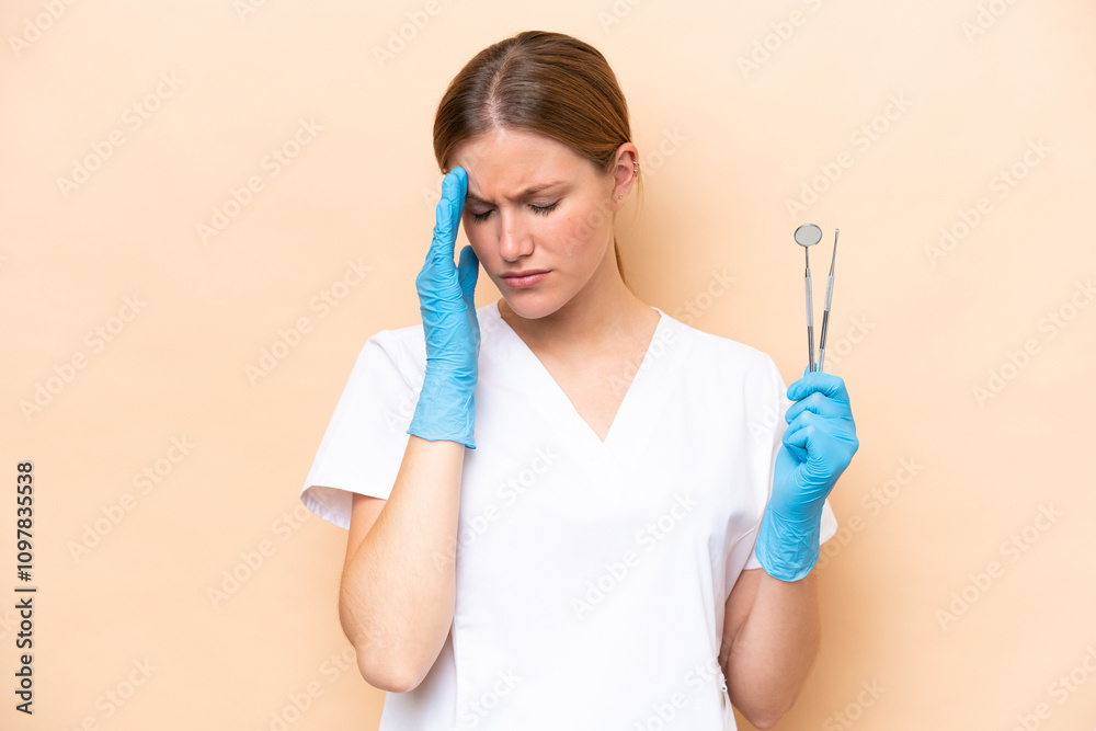 Dentist caucasian woman holding tools isolated on beige background with headache Dentist caucasian woman holding tools isolated on beige background with headache