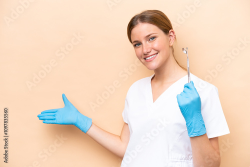 Dentist caucasian woman holding tools isolated on beige background extending hands to the side for inviting to come