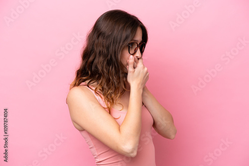 Young caucasian woman isolated on pink background covering mouth and looking to the side