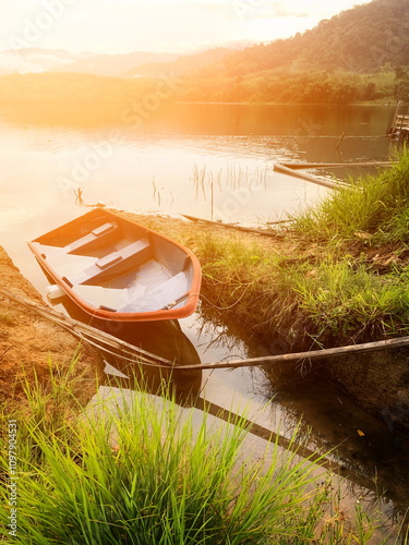 A lone boat floats on calm waters, framed by majestic mountains in the background. The warm hues of a glowing sunset cast a serene, golden ambiance over the tranquil scene.