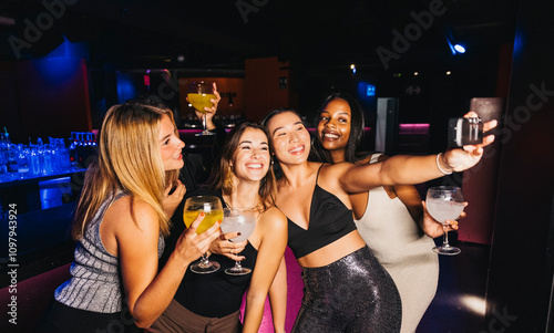A group of four young women happily take a selfie together while enjoying drinks at a vibrant party. photo