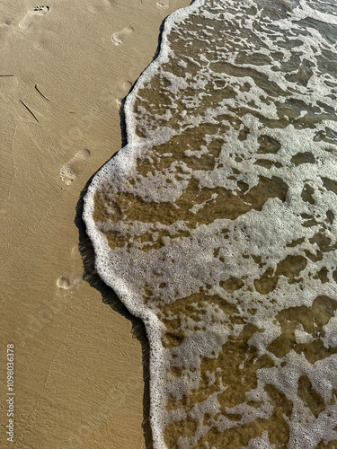 Morska fala na piaszczystej plaży z odciskami stóp photo